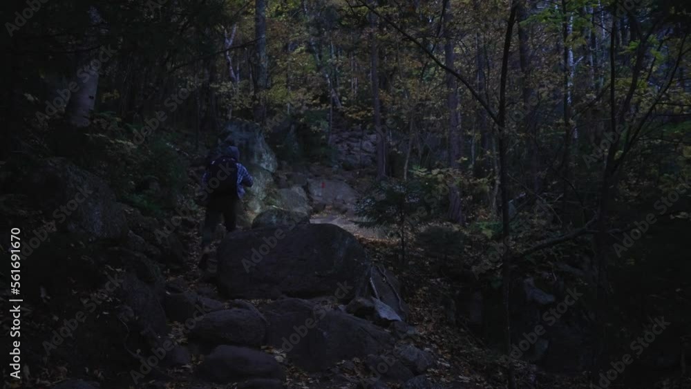 Young man hiking up a steep rocky trail in the dark with a flashlight. Hiker walks up a rocky hill in the night with a flashlight. Young man hiking up a steep rocky trail in the dark with a flashlight. Hiker walks up a rocky hill in the night with a flashlight.