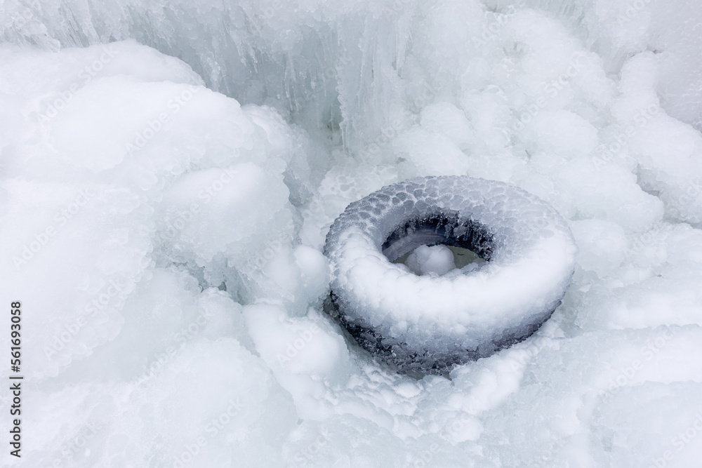 A discarded tire from a car is frozen into ice after freezing rain in winter. After the rain everything was covered with snow.