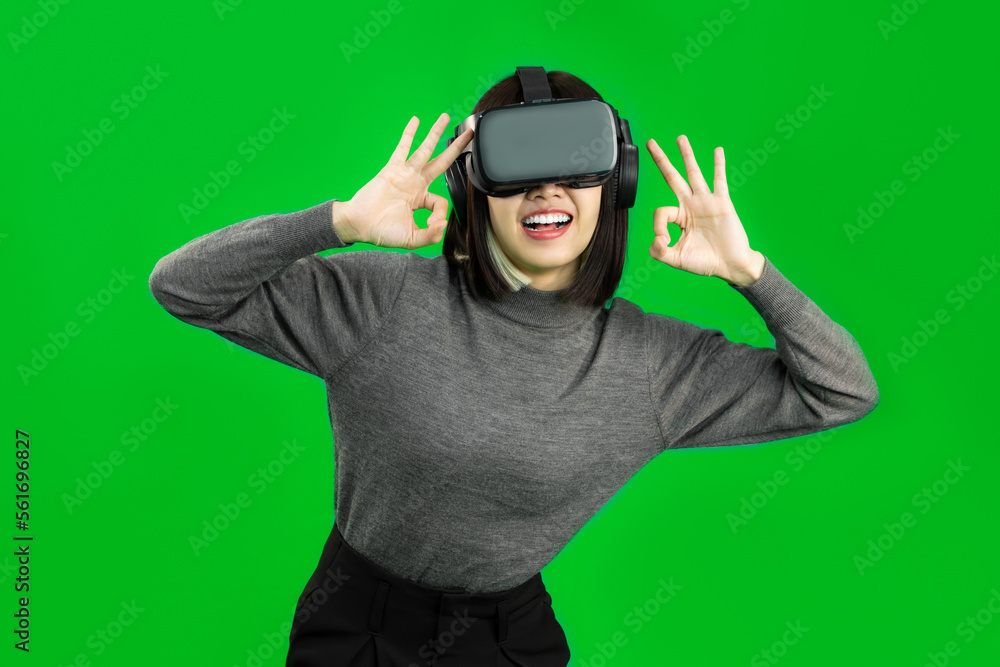 Happy Young Asian woman wearing a gray shirt and a VR headset with OK sign, greenscreen Happy Young Asian woman wearing a gray shirt and a VR headset with OK sign, greenscreen