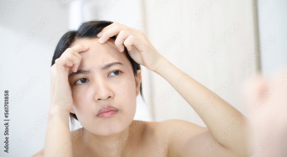 Problem skin. Concerned young asian women popping pimple on cheek while standing near mirror in bathroom. young asian women with acne Problem skin. Concerned young asian women popping pimple on cheek while standing near mirror in bathroom. young asian women with acne