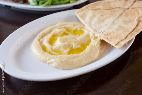 A view of a plate of hummus, with some pieces of pita bread.