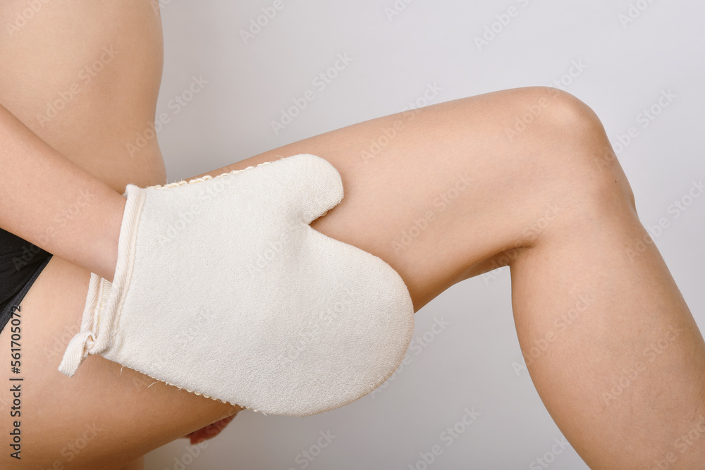 Exfoliation gloves, Dry brushing massage for anti-cellulite and lymphatic flow, Woman scrubbing leg skin.