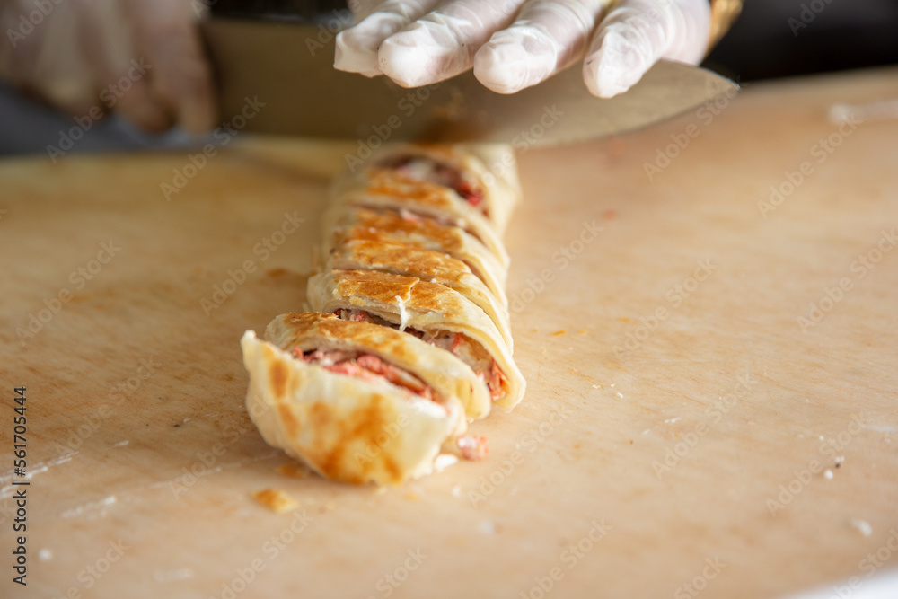 A closeup view of a cook slicing a chicken shawarma wrap at the ingredient station of a restaurant kitchen.
