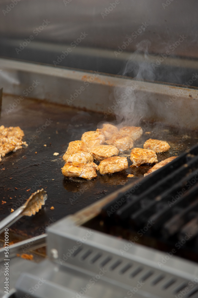 A view of several pieces of chicken kabob cooking on a restaurant griddle surface.
