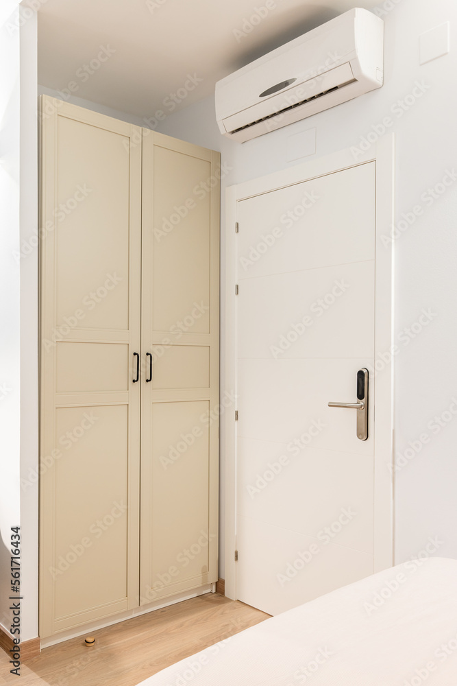 Closeup of a white wooden front door to a room next to a wardrobe. Wardrobe doors are painted beige and closed from prying eyes. Air conditioning above the door for pleasant coolness on hot nights. Closeup of a white wooden front door to a room next to a wardrobe. Wardrobe doors are painted beige and closed from prying eyes. Air conditioning above the door for pleasant coolness on hot nights.