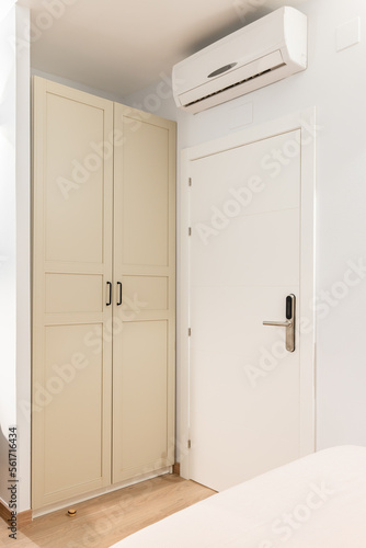 Closeup of a white wooden front door to a room next to a wardrobe. Wardrobe doors are painted beige and closed from prying eyes. Air conditioning above the door for pleasant coolness on hot nights.