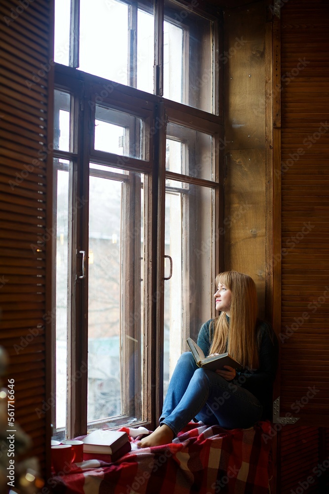 Dreamy girl sits on a window with a book