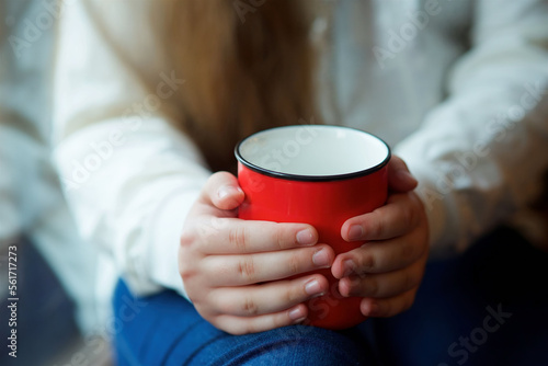 A cup of hot drink in the hands of a girl.