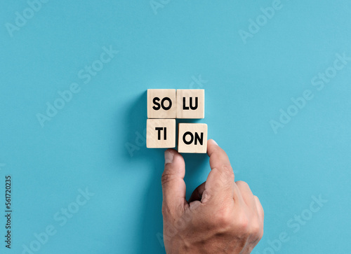 Finding a solution to a problem in business. Male hand placing wooden blocks into a square shape to assemble the word Solution.