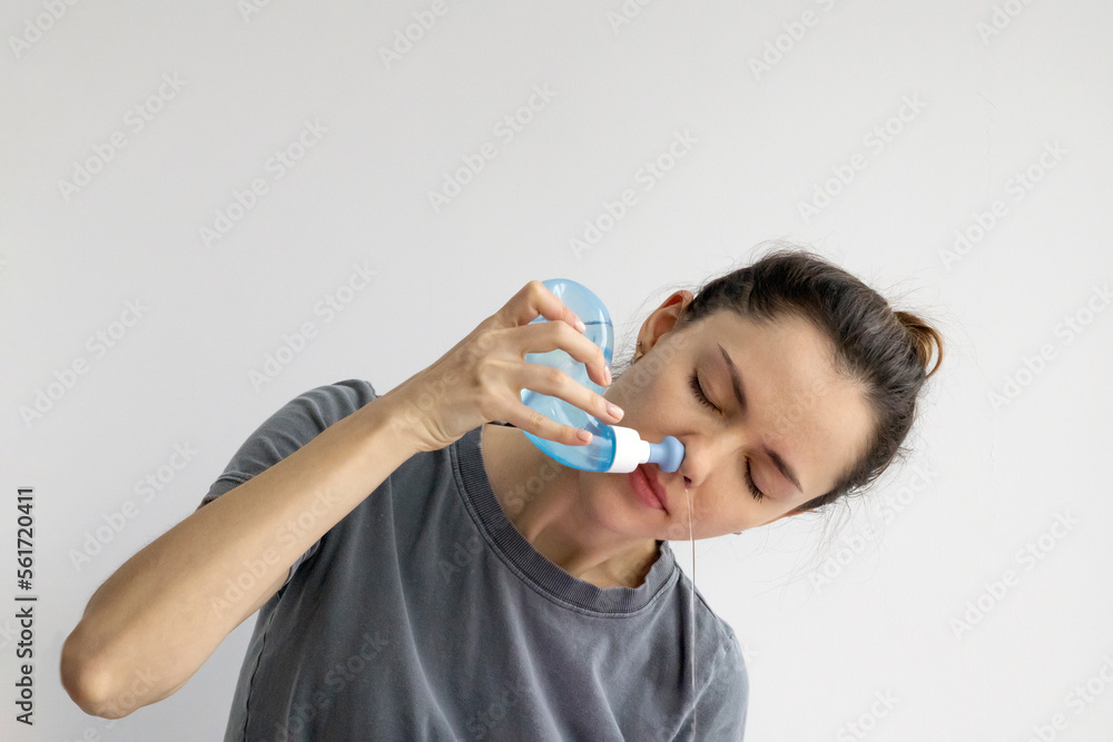 Girl rinses her nose with saline solution at home Using Neti Pot. Treatment and prevention of colds. How to rinse your nose when you have a runny nose. - obrazy, fototapety, plakaty 