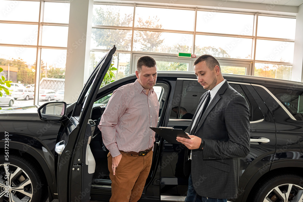 friendly salesman with male client talking and explaining new car before sale or rent in dealership friendly salesman with male client talking and explaining new car before sale or rent in dealership