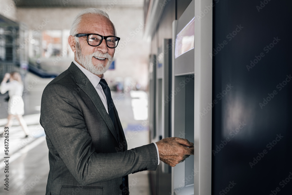 Portrait of smiling male professional withdrawing money through ATM machine. Elderly entrepreneur using electronic banking Portrait of smiling male professional withdrawing money through ATM machine. Elderly entrepreneur using electronic banking
