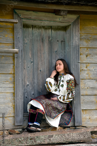 Ukrainian girl in national hutsul clothes sits on the threshold of an old wooden house photo