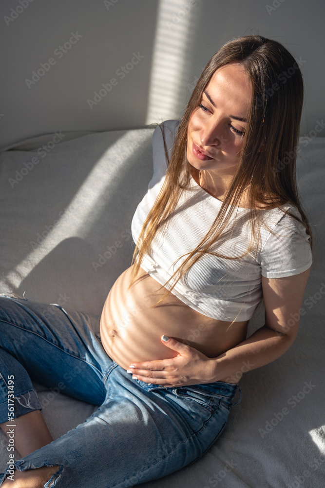 Pregnant woman on the bed in the room on a sunny morning.