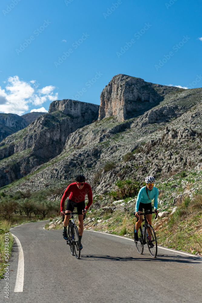 Mature cyclists together riding bicycles on road in front of rocks Mature cyclists together riding bicycles on road in front of rocks