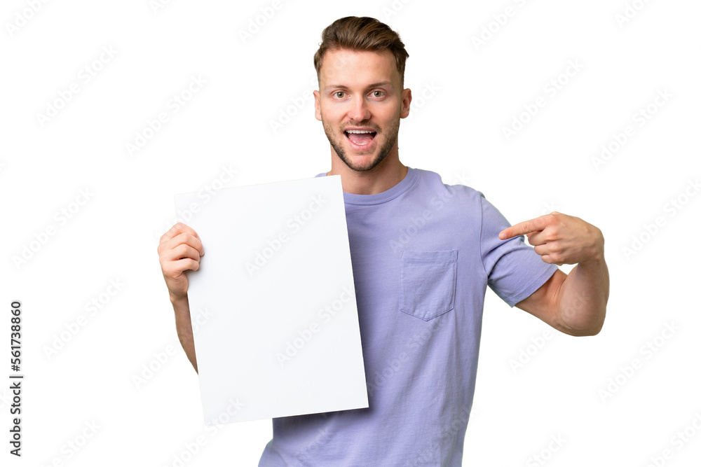 Young blonde caucasian man over isolated background holding an empty placard with happy expression and pointing it Young blonde caucasian man over isolated background holding an empty placard with happy expression and pointing it
