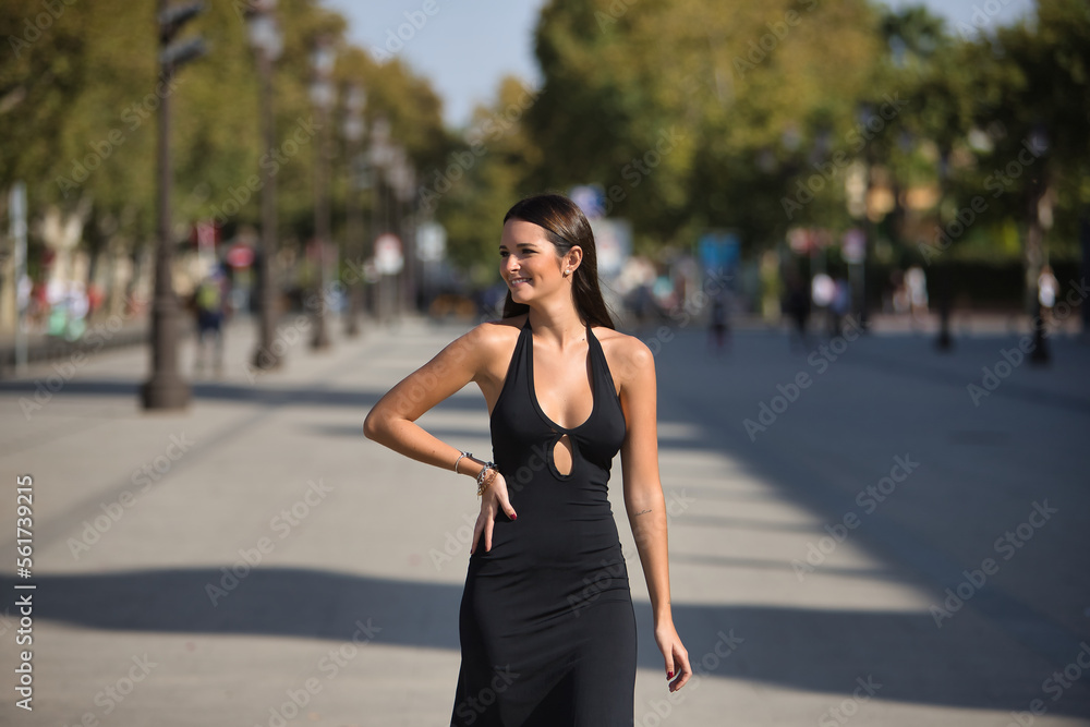 Young and beautiful woman with straight brown hair, wearing an elegant black dress, walking downtown, empowered and independent, smiling and happy. Concept fashion, beauty, empowerment, millennial.
