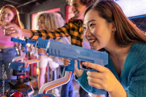 Happy young woman enjoying shooting game with friends at arcade photo
