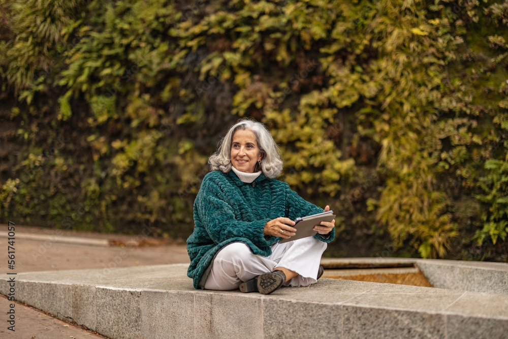 Happy senior woman sitting with tablet PC in front of plants