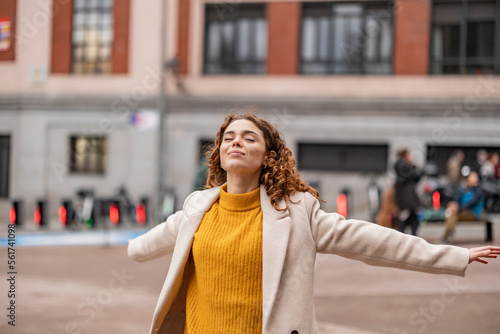 Carefree young woman with arms outstretched standing on footpath photo