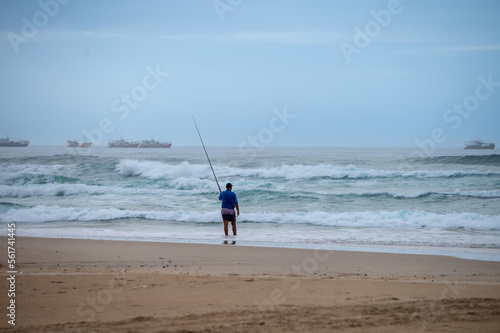 Rear view of man seen fishing along coast