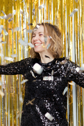 Happy woman wearing black dress under falling confetti in new year's party