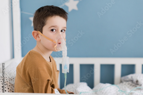 Sick boy wearing nebulizer mask sitting on bed at home