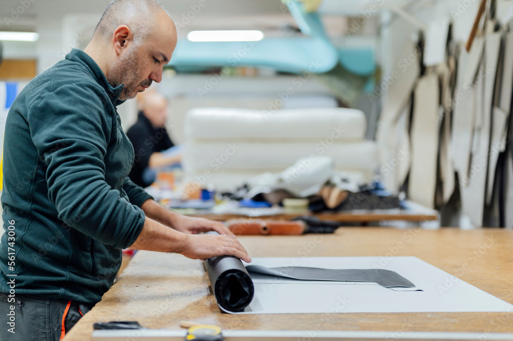 Upholstery worker rolling fabric by table in workshop Upholstery worker rolling fabric by table in workshop