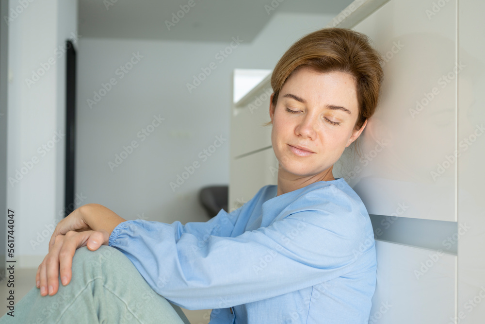 Woman with eyes closed resting in front of cabinets in kitchen Woman with eyes closed resting in front of cabinets in kitchen