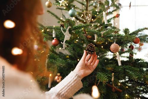 Hand of woman touching pine cone hanging on Christmas tree at home