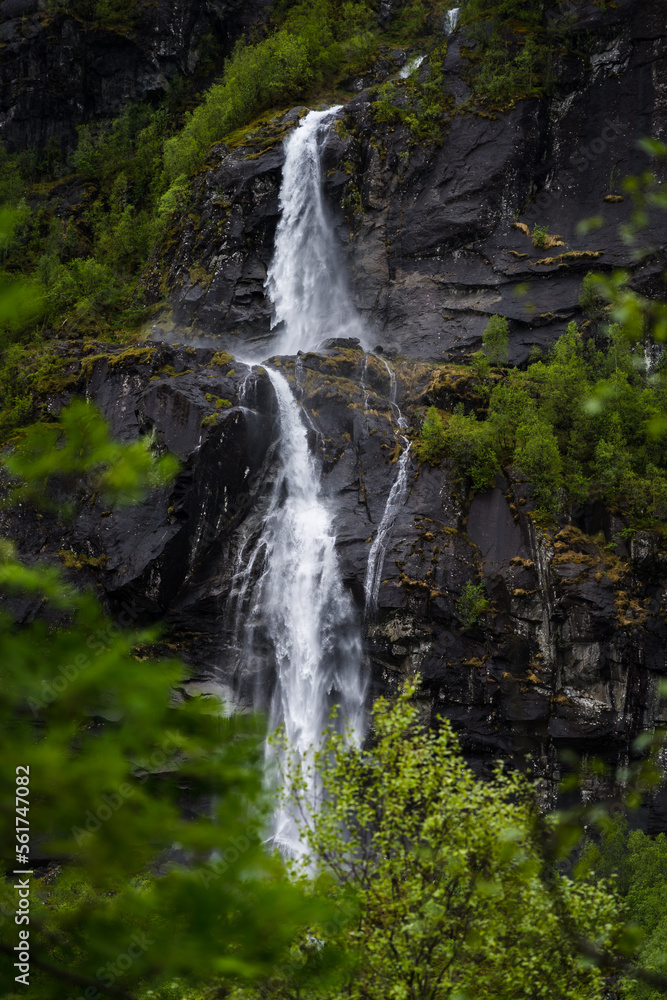 Waterfall in Norway on a steep mountain with trees in the foreground