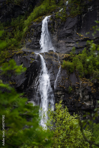 Waterfall in Norway on a steep mountain with trees in the foreground