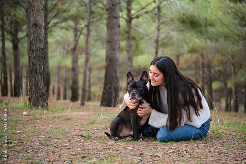 Young caucasian woman hugging her mixed breed dog at a pine forest.