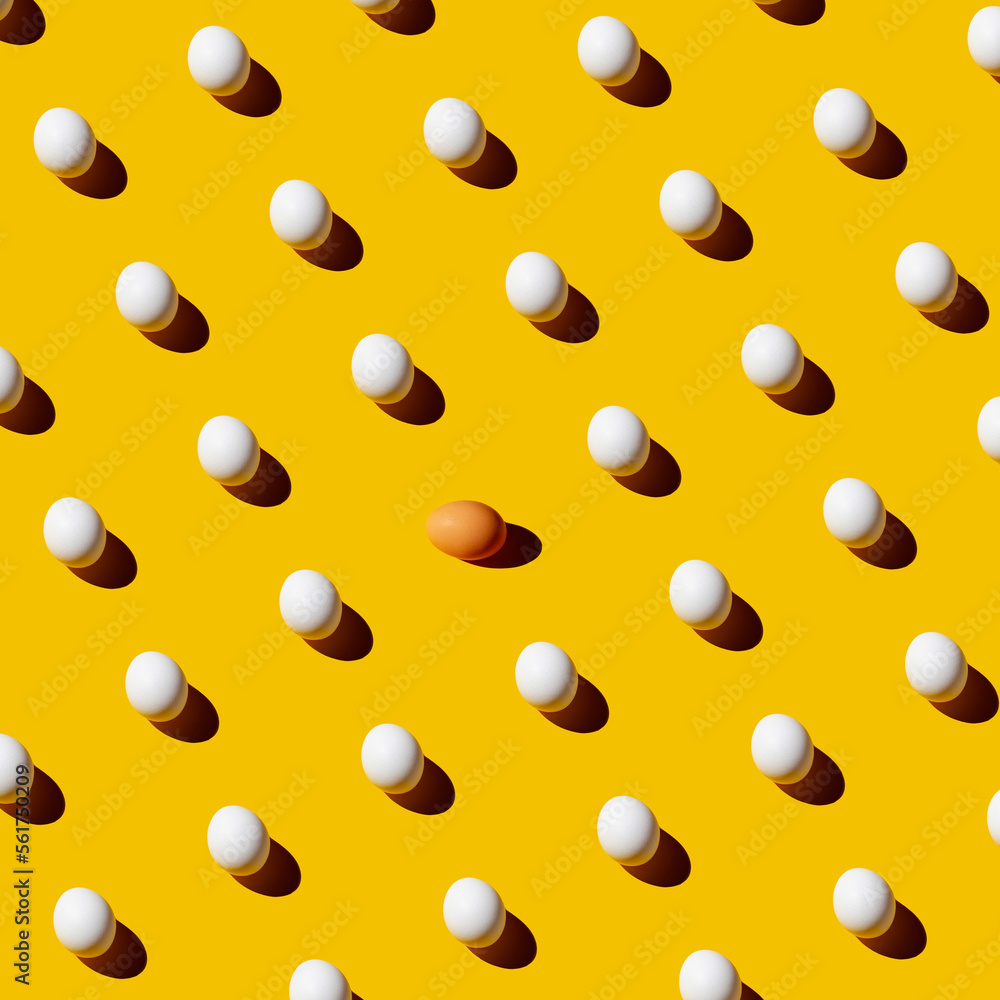 Chicken white eggs pattern on yellow background with one brown egg in the middle. Different concept. Chicken white eggs pattern on yellow background with one brown egg in the middle. Different concept.