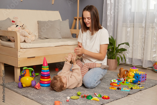 Indoor shot of young beautiful mother playing and having fun on the floor with her little daughter, mom and kid clapping hands, play games, singing nursery rhymes and finger gymnastics. photo