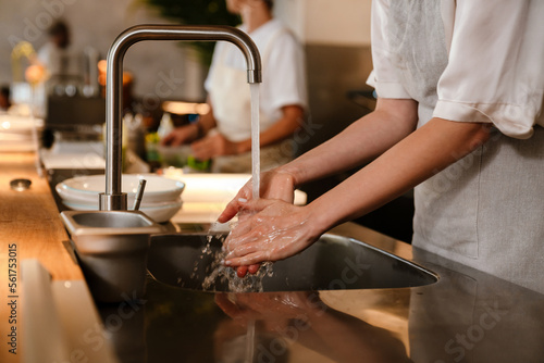 Young chef woman washing hands while working in restaurant kitchen