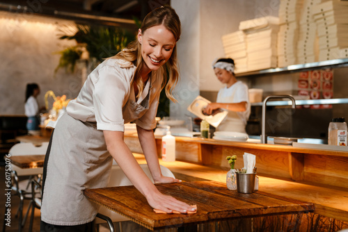 Young woman wearing apron cleaning table while working in restaurant
