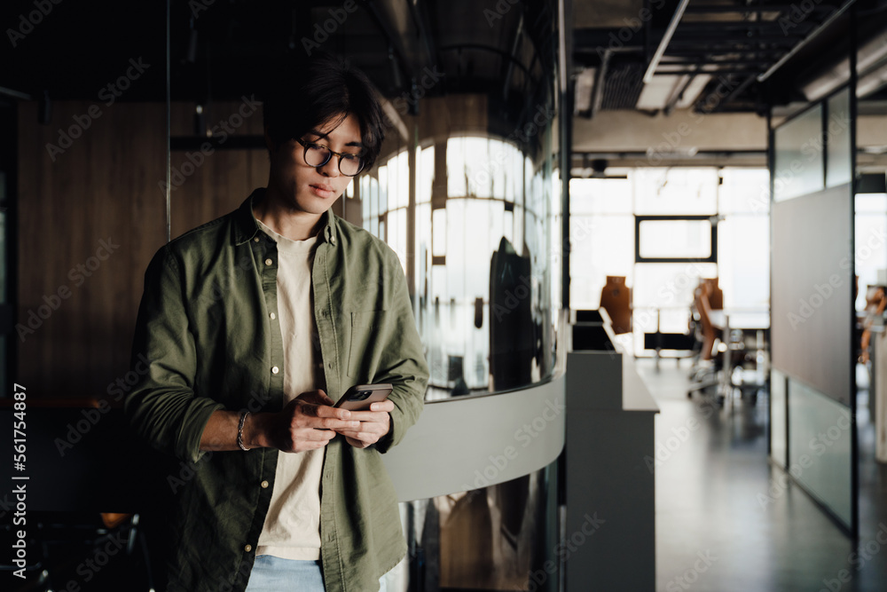 Young business man using smartphone while standing in modern office space Young business man using smartphone while standing in modern office space