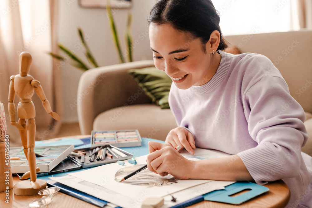 Smiling asian woman artist drawing with pencil while sitting at home Smiling asian woman artist drawing with pencil while sitting at home