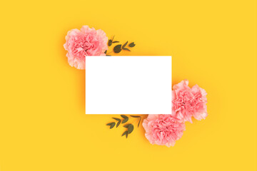Empty paper card mock up, pink carnation flowers and green eucalyptus branches on a yellow background. Place for text.