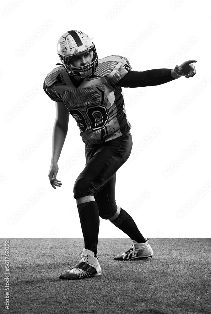 Black and white photo. Man, professional american football player in uniform posing over white studio background with grass flooring. Concept of sport, competition Black and white photo. Man, professional american football player in uniform posing over white studio background with grass flooring. Concept of sport, competition