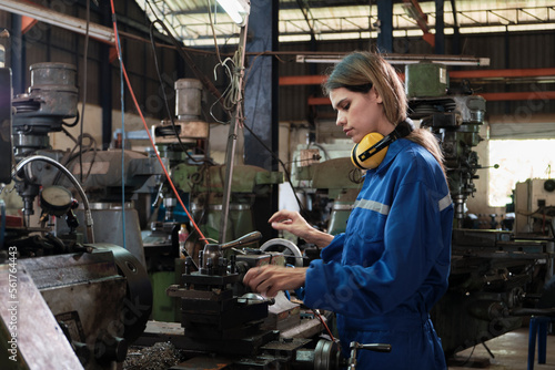 An industrial worker in protective and safety uniform and hardhat, young Caucasian female engineer works with metalwork machine in manufacturing factory. Professional production mechanical occupation.