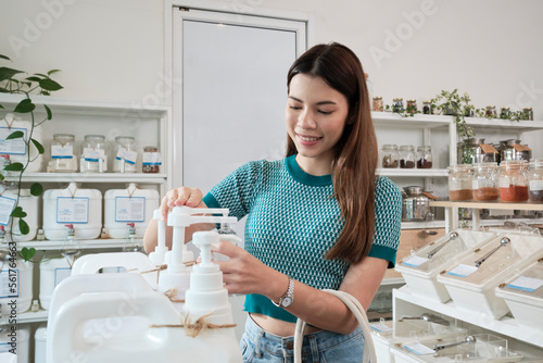 A Caucasian female customer pressed a reusable container to fill liquid products to recycle bottles at zero-waste and refill store  environment-friendly groceries  and sustainable shopping lifestyle.