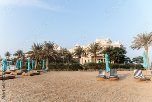 Beautiful empty beach with umbrellas and wooden sun loungers. A perfect place for a summer vacation. Dawn on an empty beach with the sea and buildings as a backdrop. 