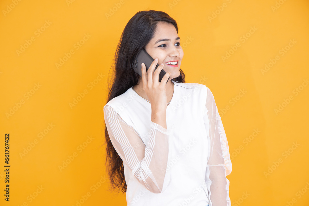 Young happy indian girl talking on her mobile phone isolated over yellow orange background. Studio Shots. Young happy indian girl talking on her mobile phone isolated over yellow orange background. Studio Shots.