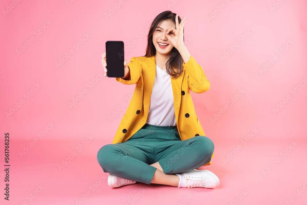 Image of young Asian businesswoman sitting and holding smartphone on background Image of young Asian businesswoman sitting and holding smartphone on background