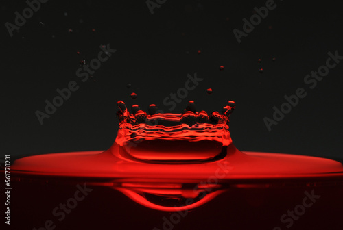 A drop of red water forming a coronet as it splashes into a glass full of liquid, backlit for contrast. photo