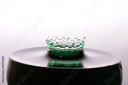 A drop of green water forming a coronet as it splashes into a glass full of liquid photo