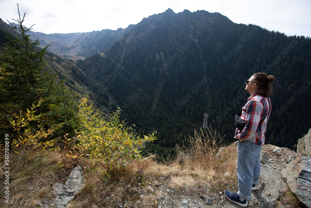 Fototapeta premium casual guy with tied hair and dark glasses looking at the mountains on a sunny day. view from behind. sunny mountains panorama