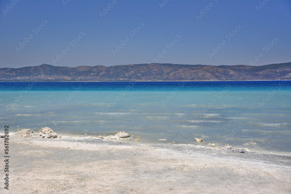 idyllic beach with white sand and blue water with mountains and clear sky on background